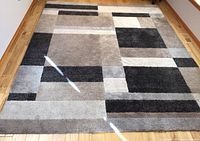 Full view of the rectangular 8x10 area rug on wooden floor showing the geometric squares pattern in gray, beige, and black colors.