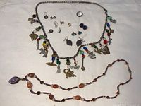 Full lot overview showing charm necklace with colorful charms, beaded necklace, and several rings and earrings spread out