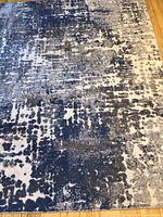 Full view of the Torino area rug showing the blue and gray distressed abstract pattern over wooden floor.