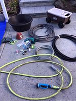 Photo showing hoses, garden tub, garden hose cart, and assorted garden accessories spread out on concrete ground.