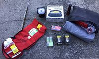 Photo showing all camping supplies including first aid kit, electric burner box, candle lanterns, binoculars, and air mattress.