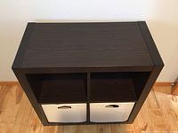 Frontal view of dark laminate cube shelf with two light colored fabric storage bins in bottom compartments