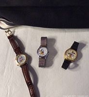 Photo of three wristwatches featuring Mickey Mouse on the dial, with different strap materials and bezel colors