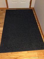 Top view of large dark blue entry rug with subtle textured pattern on surface, placed on hardwood floor.