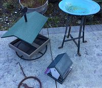 Portable bird feeder with green roof and black bird figure, blue metal bird bath with slender legs, small bird house with green roof.