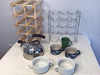 Two wine racks, stainless steel kettle, two ceramic mugs, and two white dishes arranged for lot display