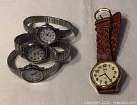 Photo showing three ladies watches with silver metal expansion bands stacked together and one carriage style watch with braided brown leather band to the side.