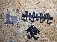 Photo of three metal animal-themed wall hooks including a two-birds hook, a five-cats hook, and two small cat-shaped hide-a-key boxes on a granite surface.