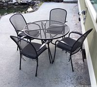 Wide shot of gray metal mesh patio table with four chairs on concrete surface.