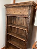 Full front view of carved bookshelf showing three shelves and carved decorative panel at top