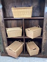 Five wicker rectangular picnic baskets arranged in a wooden shelving unit, showing front and side views with lids closed.