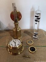 Overview of all five items arranged on table: lantern, clock, thermometer, compass ring and dial, whistle