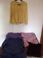 Yellow v-neck sweater hanging with five additional sweaters laid flat on table