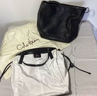 Two handbags and a Cole Haan dust bag: black Cole Haan tote at top and white Burberry handbag below.