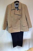 Tan cotton double-breasted jacket with navy piping and dark jeans hanging on wall