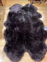 Full view of chocolate brown shaggy sheepskin rug laid out on hardwood floor