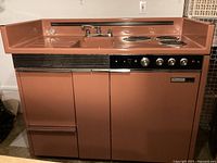 Front view of kitchenette showing sink, burners, control panel, and refrigeration compartment