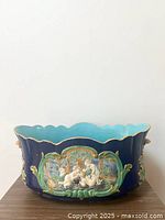 Front view of heavy ceramic planter showing scalloped rim and decorative cherub relief on blue background