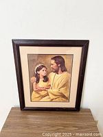 Framed picture of Jesus holding a young girl, showing the artwork and wooden frame with minor wear.