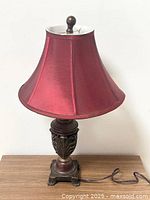 Front view of the wooden table lamp showing the red fabric lampshade and decorative carved wooden base with claw feet.