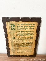 Front view of wooden plaque showing scripture passage and scalloped edges with visible wear.