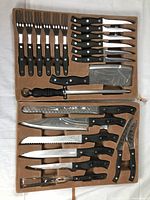 Full set laid in original tan case showing all knives and forks with black handles and stainless steel blades