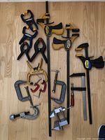 Top-down photo showing full lot of 18 clamps and clamping tools on wood floor