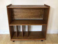 Front view of the wood entertainment stand showing shelves and vertical dividers on wheels.