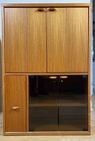 Front angle view of wooden entertainment unit showing two folding doors on top and glass doors below with wooden handles.