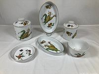 Photo showing two oval baking dishes, bowl, two canisters with lids, and a small dish decorated with Evesham vegetable and fruit designs with gold trim