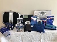 Overview photo showing all home health items including massagers, scales, blood pressure monitors, compression stockings, and cold gel packs arranged on a white surface