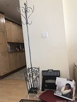 Full view of metal coat tree with umbrella holder, new boxed ObusForme travel neck pillow, black folding step stool, burgundy shoe rack tray, and door mat against a beige wall and kitchen background.