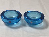 Pair of thick round teal blue glass candle holders with Iittala logo stickers visible on the side. View shows the concave top to hold tealight candles.