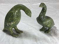 Two green stone bird sculptures shown side by side on white cloth background