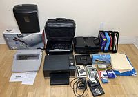 Full lot overview showing assorted office equipment and supplies including printers, typewriter, shredder, calculators, folders, and bags.