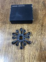 Top view of vintage iron candlestick holder showing radial design with 12 spokes and candle sockets, alongside original black box with 'Dansk Designs' labeling.