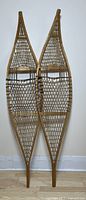 Pair of wooden traditional snowshoes standing upright against a wall, showing full front view.