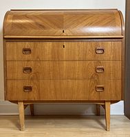 Front view showing tambour roll-top closed over writing area and three drawers with recessed handles