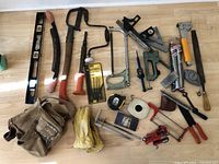 Overview of lot showing all vintage hand tools laid out on floor including tool bag, gloves, saws, clamps, measuring tapes, and other tools.