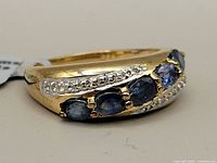 Close-up side view of gold rhodium plated ring with five blue sapphires and white topaz accent stones.