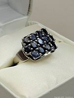 Close-up angled view of the silver rhodium plated ring featuring a cluster of deep blue sapphire stones set in a rectangular pattern.