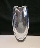 Front view of the clear glass tulip vase on a white surface with black background.