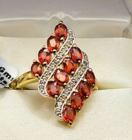 Close-up of the ring showing orange oval sapphires and two wavy lines of white topaz stones on top, gold rhodium plated silver band.