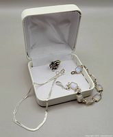 Photo showing the sterling silver necklace, silver pendant, and bracelet with white stones inside a white jewelry box.