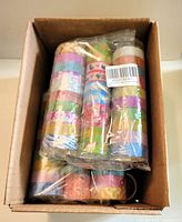 Box filled with multiple packs of layered washi tape rolls, some sealed in plastic packaging.