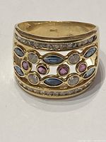 Front view of ring showing channel-set outer rows of clear stones and center openwork band with marquise blue and round pink/clear stones