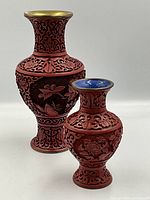 Two ornately carved cinnabar vases, one larger with brass interior and the other smaller with blue enamel interior and brass rim