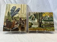 Two paintings on clear acrylic easels against white backdrop