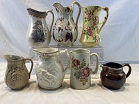 Seven handcrafted decorative pitchers arranged in two tiers showing size and design details.