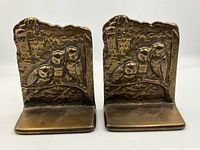 Front view of the pair of brass bookends with embossed three perched owls and castle background, showing the patinated finish and detailing.